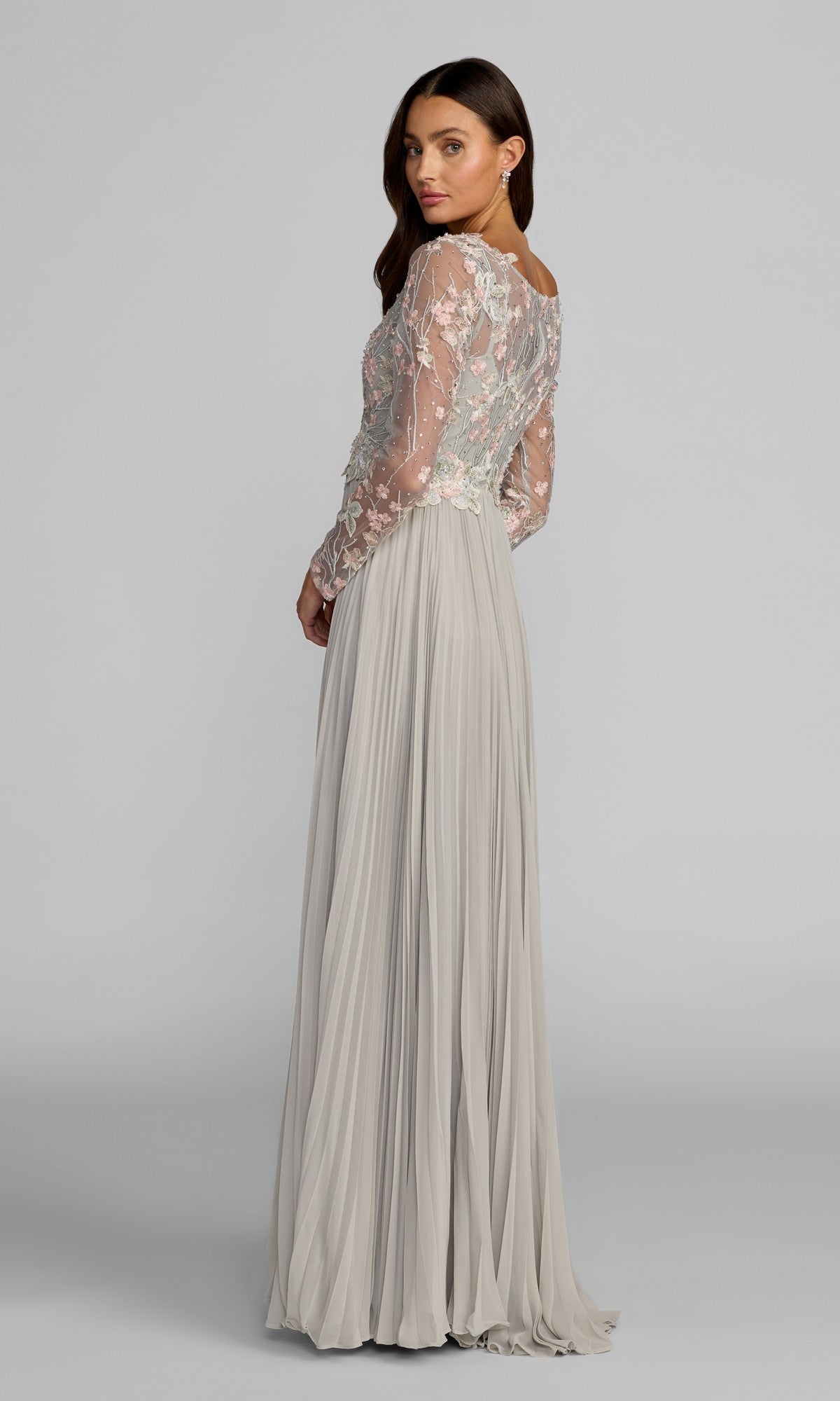 A woman wearing the Mac Duggal 21332 long formal dress, which features a sheer, floral-embroidered bodice and a flowing light gray chiffon A-line skirt, stands and looks over her shoulder against a plain background.